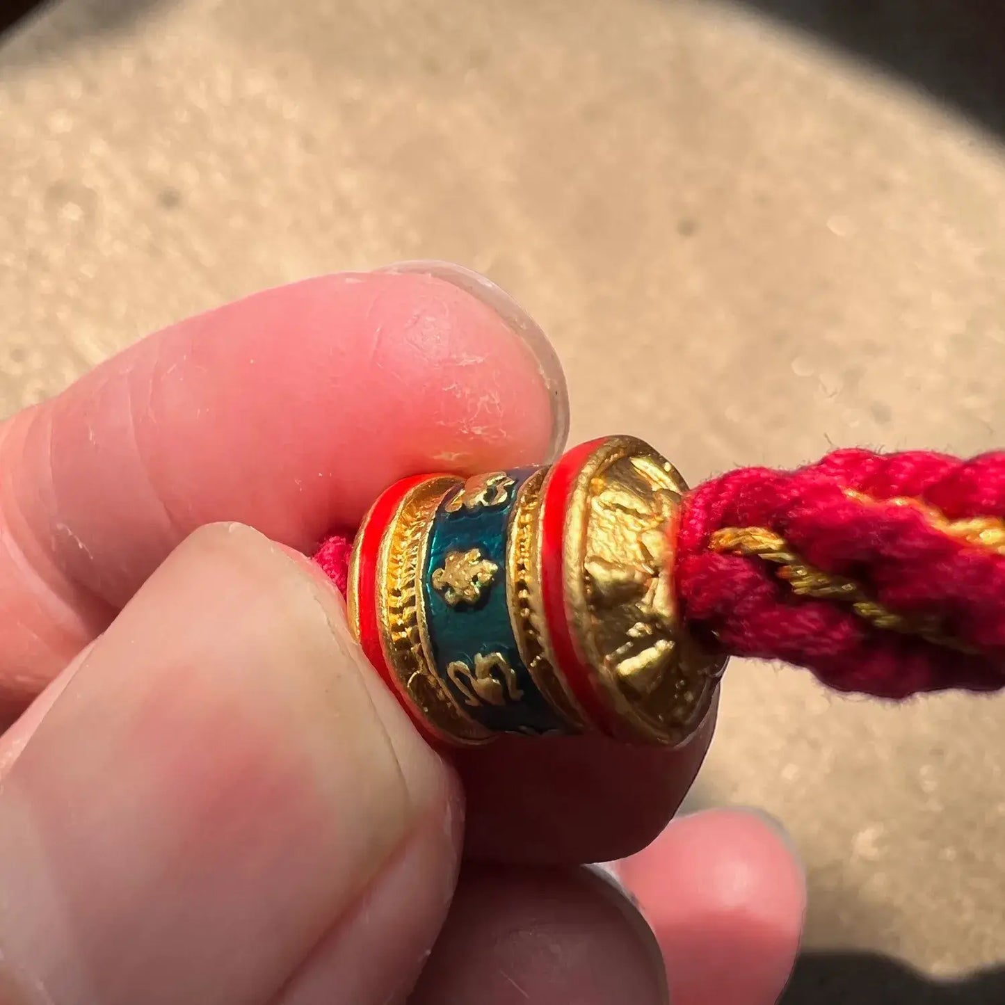 Close-up of a red string bracelet with a gold and blue charm held between fingers.