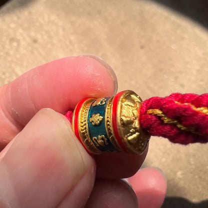 Close-up of a red string bracelet with a gold and blue charm held between fingers.
