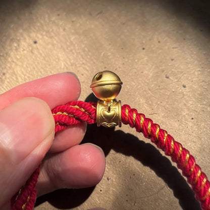 Red and gold braided cord with a decorative gold clasp held by a hand on a beige surface.