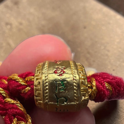 Gold charm with red string held between fingers on a neutral background