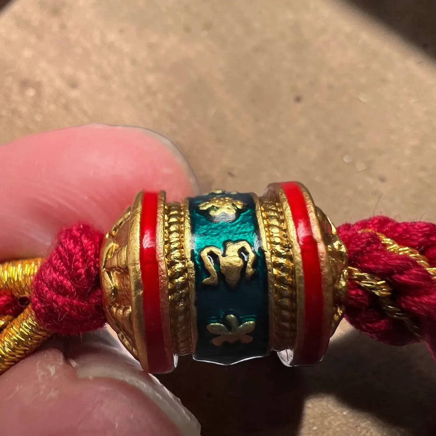 Decorative beaded charm with red and gold threads held by a hand against a neutral background