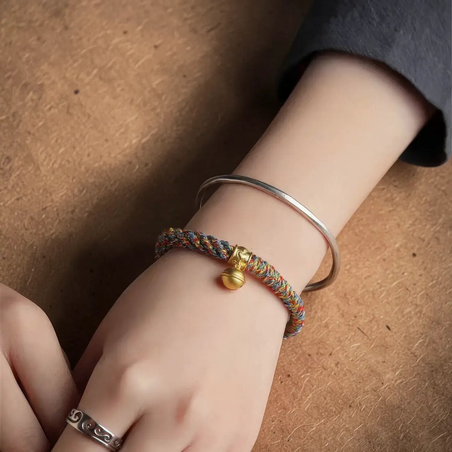 Close-up of a wrist wearing a colorful braided bracelet with a gold charm on a brown surface.