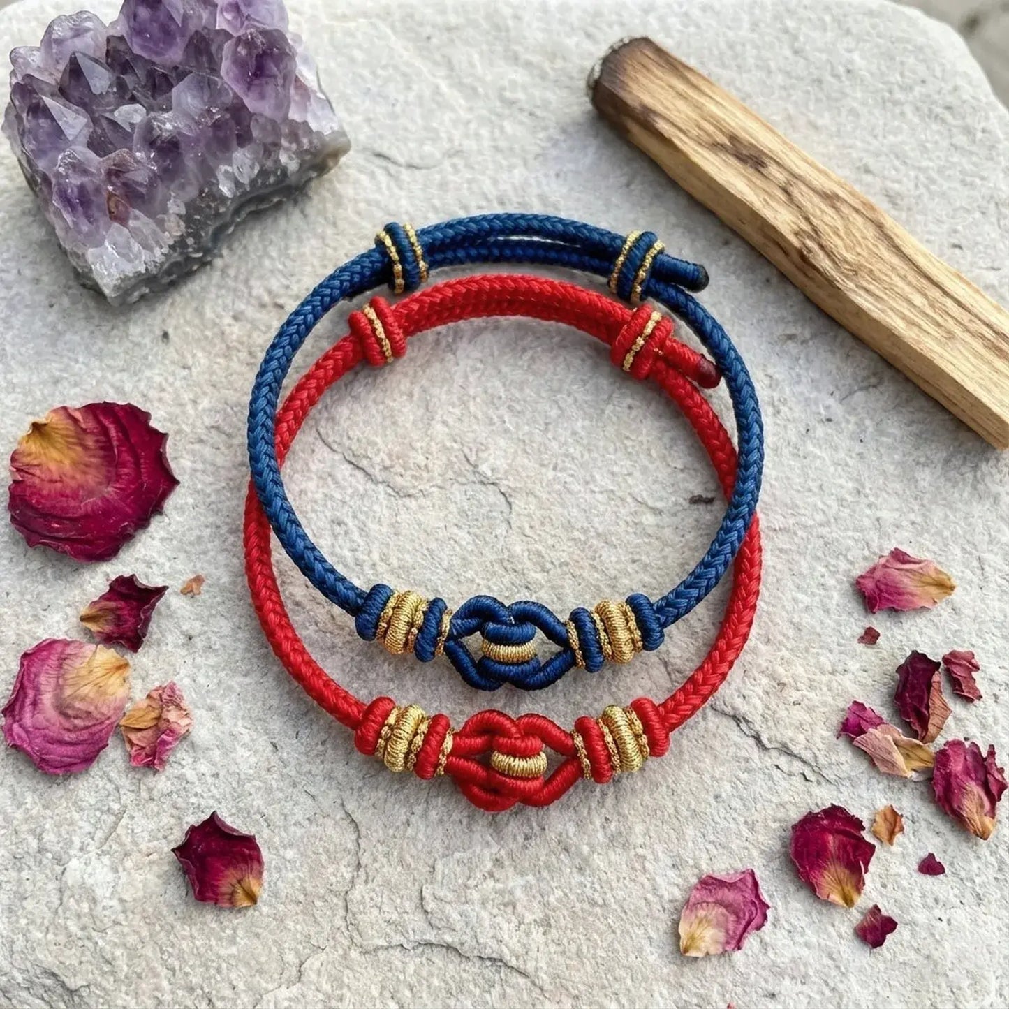 Red and blue bracelets with gold accents on a stone surface with dried flowers and a crystal.