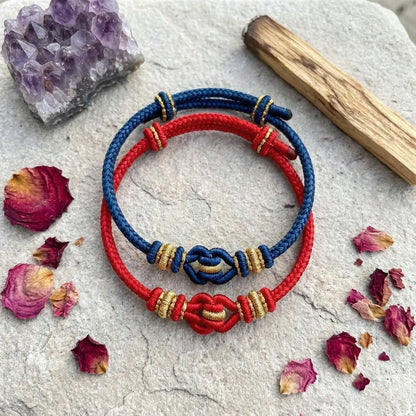 Red and blue bracelets with gold accents on a stone surface with dried flowers and a crystal.