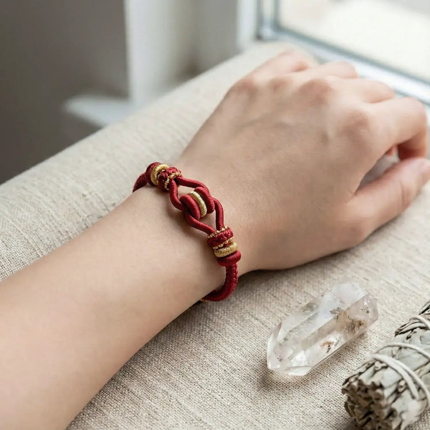 Hand wearing a red bracelet with gold accents on a textured surface.