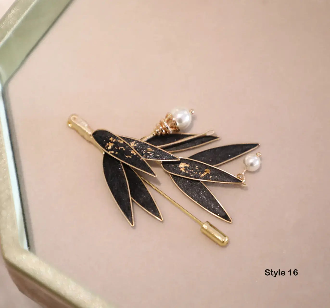 Black leaf-shaped brooch with gold accents and pearls on a pink background