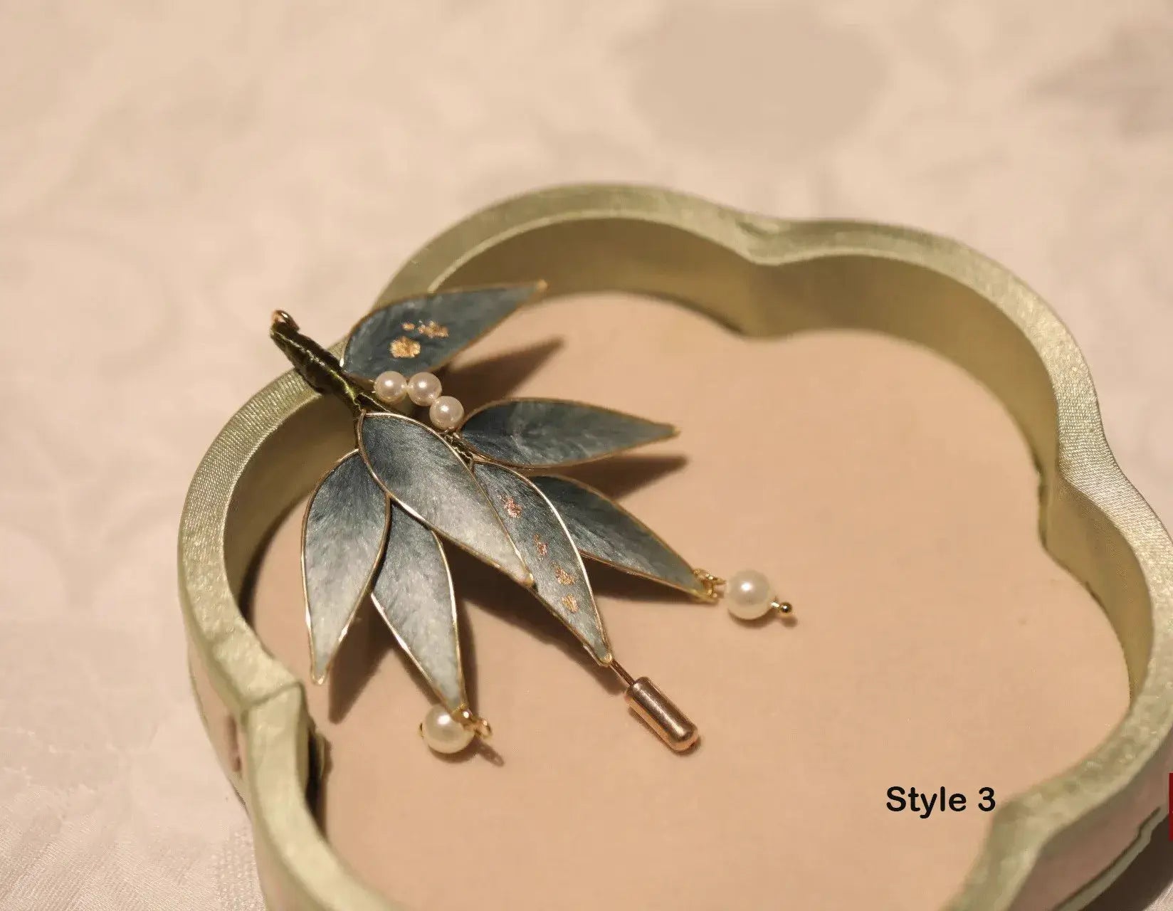 Decorative hair clip with leaf and pearl design on a beige background