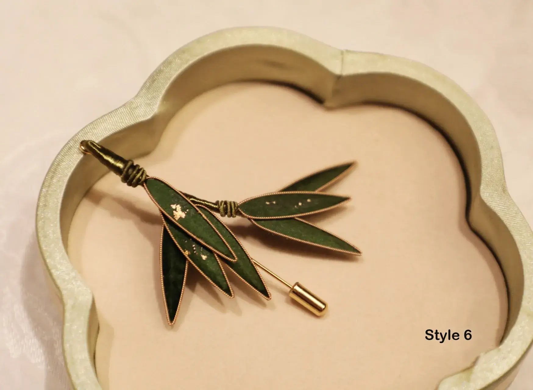 Brooch with green leaves and gold accents on a heart-shaped cushion