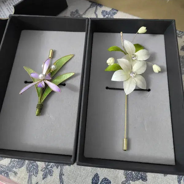 Two floral pins in a black box on a patterned surface