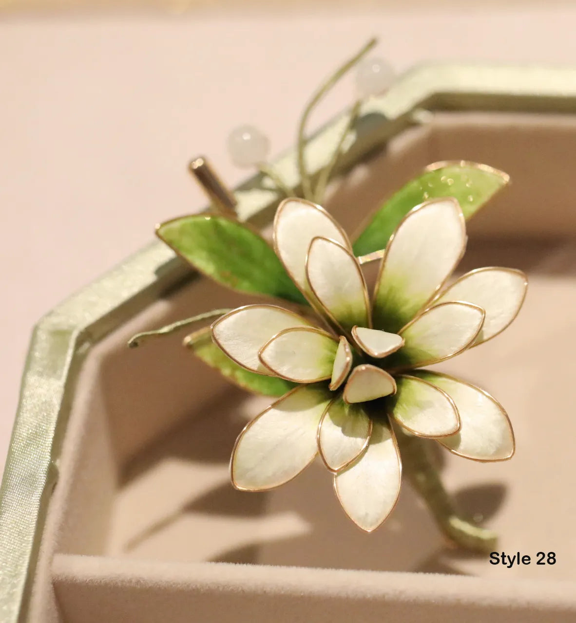 Floral brooch with green and white leaves on a pink background