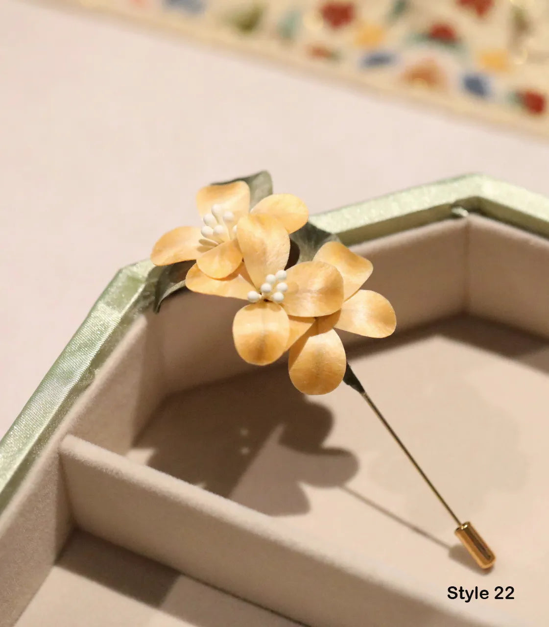 Gold flower-shaped brooch with pearl center on a beige background