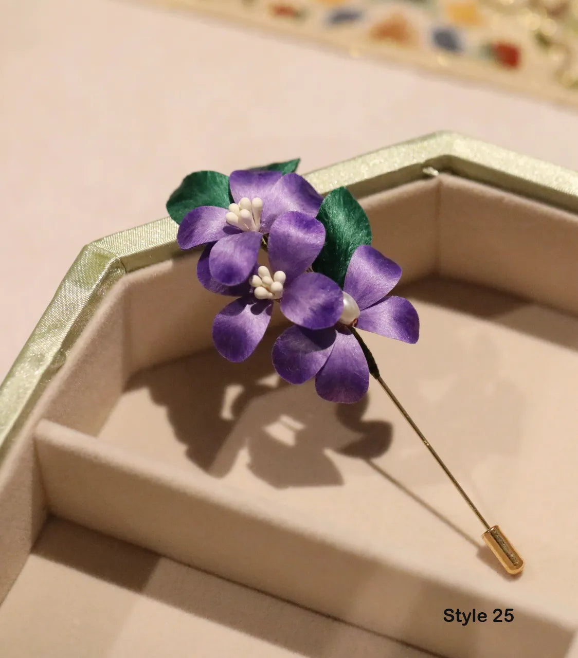 Purple flower-shaped brooch with green leaves on a beige background