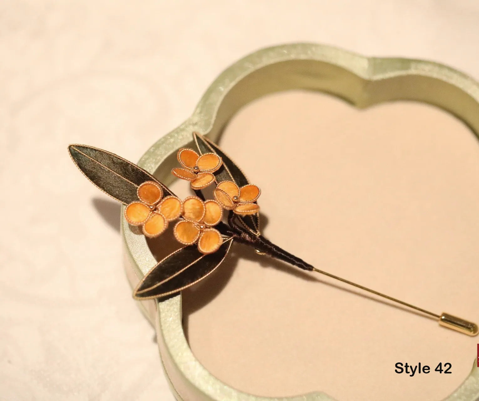 Floral brooch with orange flowers and green leaves on a beige background