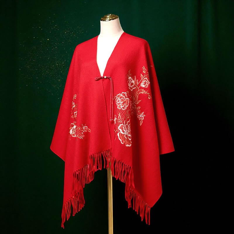 Red poncho with white floral embroidery on a mannequin against a dark green background
