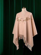 Beige poncho with floral embroidery and fringes on a mannequin against a green curtain background