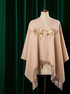 Beige poncho with floral embroidery and fringe on a mannequin against a green curtain background