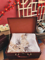 Embroidered fabric in an open brown suitcase with a decorative background