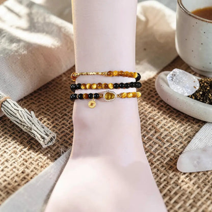Three beaded bracelets styled on a pale pink wrist form, set against a rustic burlap background with a ceramic cup, crystals, and a tassel.
