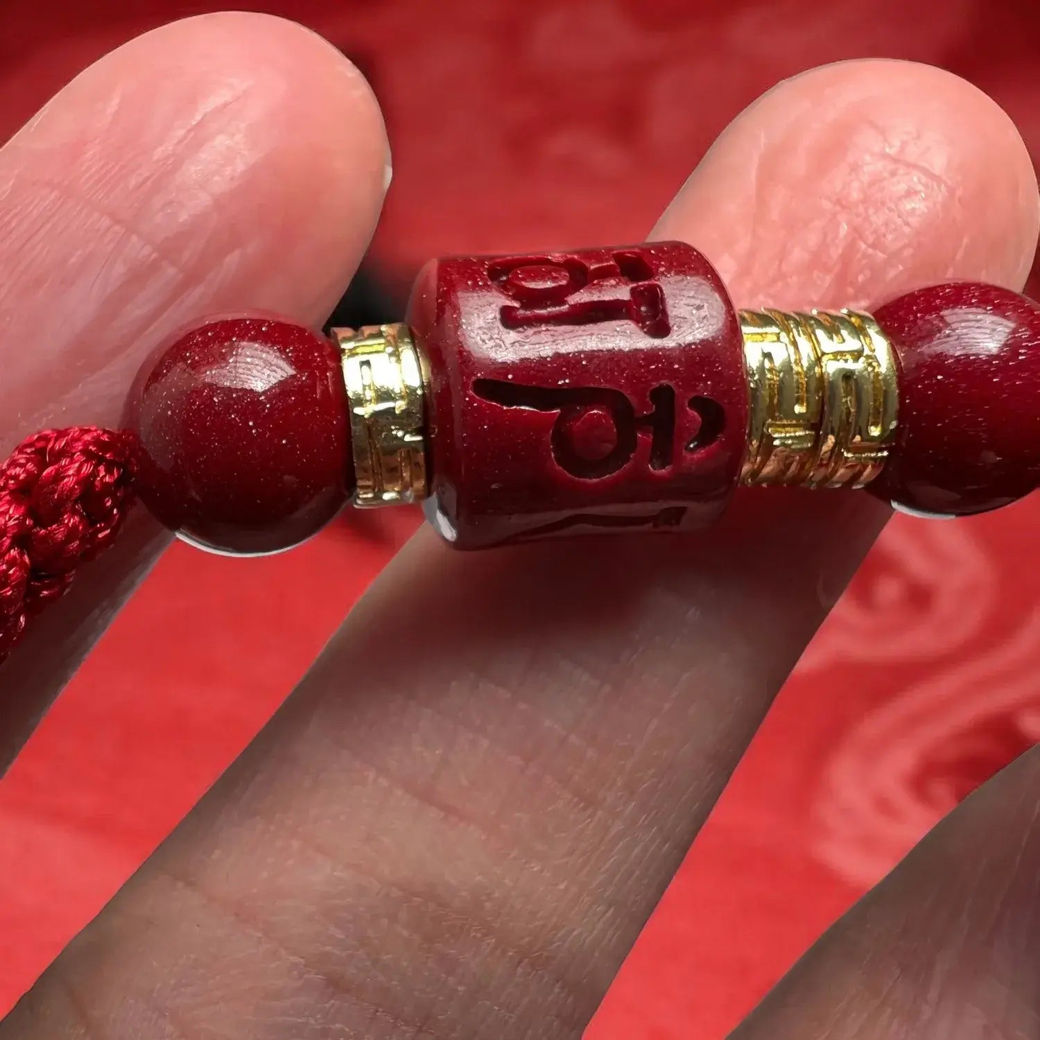 Close-up of a red beaded bracelet with gold accents held between fingers against a red background.