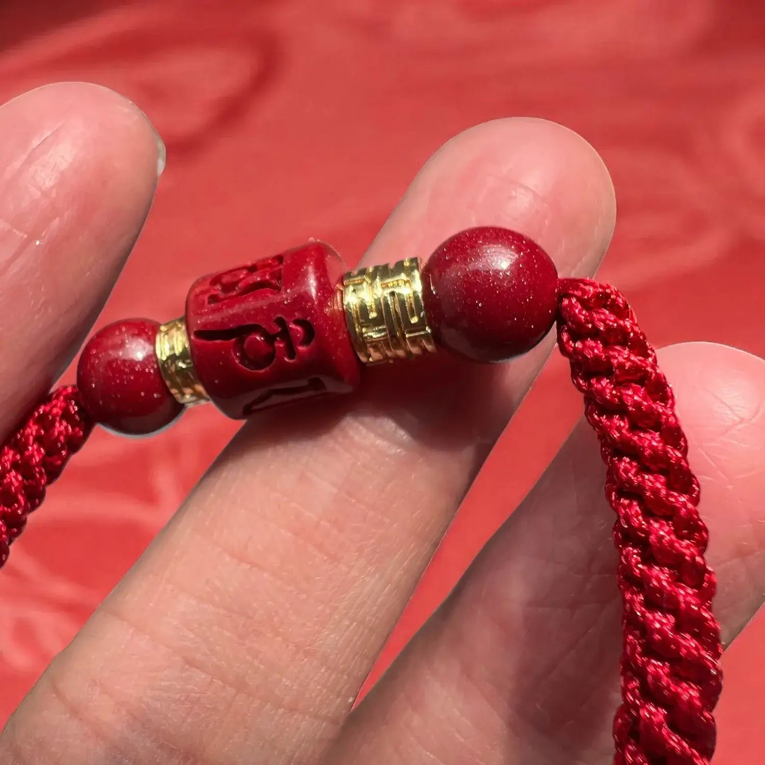 Red beaded bracelet with gold accents held between fingers against a red background