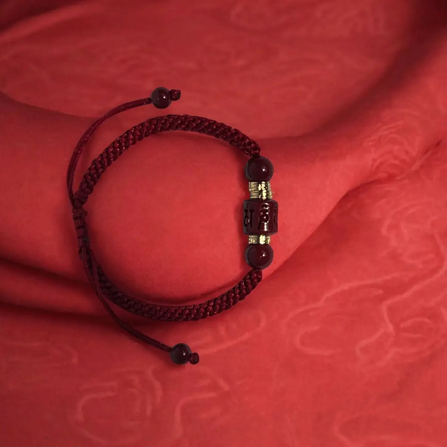 Red braided bracelet with beads on a red textured fabric background