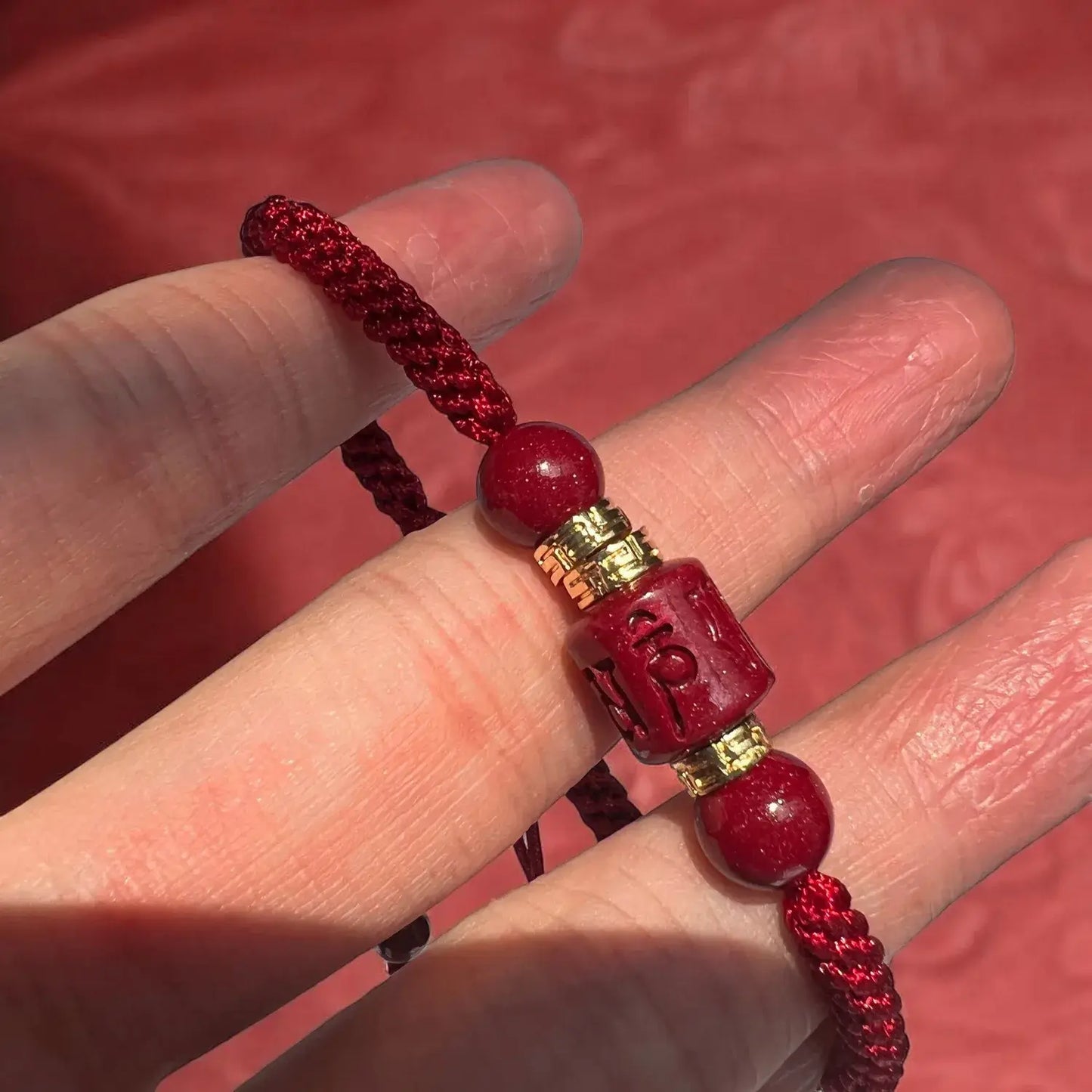 Red beaded bracelet with gold accents held between fingers against a red background