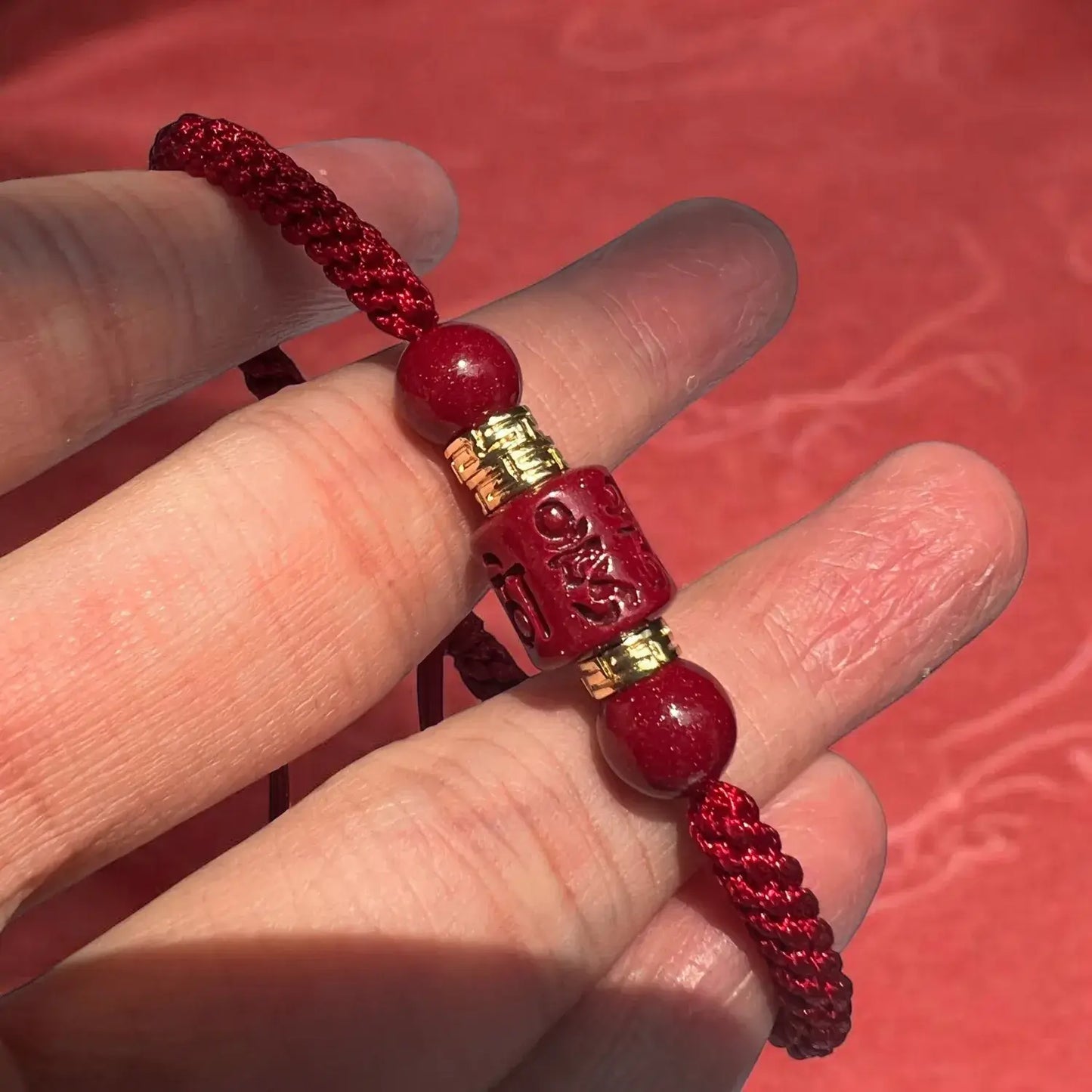 Red beaded bracelet with a gold clasp held between fingers against a red background