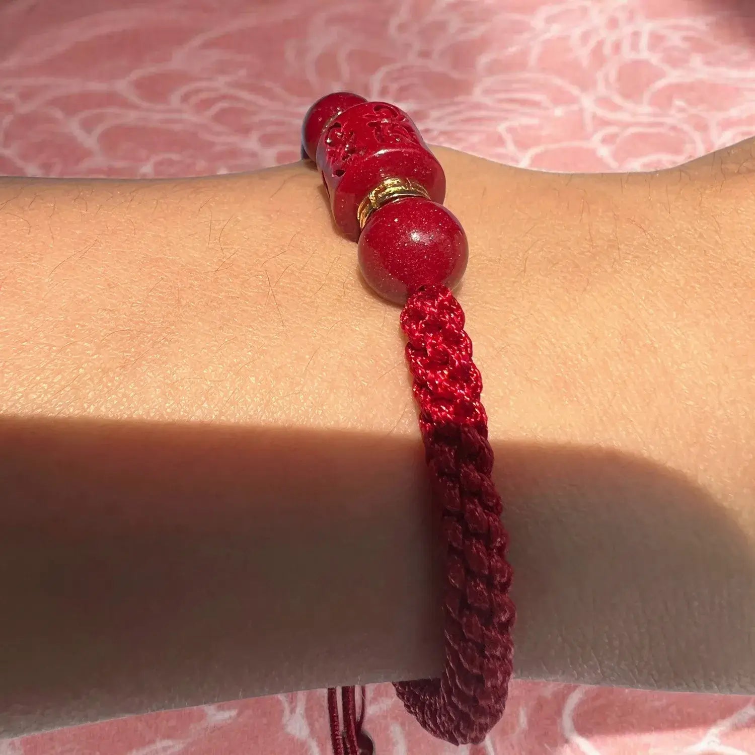 Red beaded bracelet on a wrist with a pink textured background