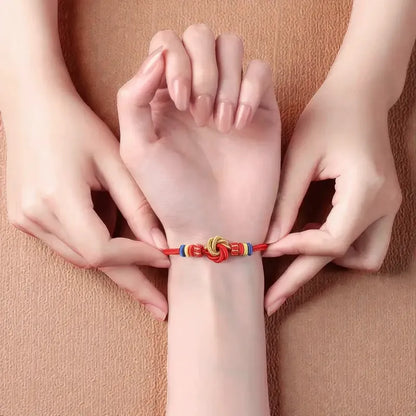Three hands holding a wrist with a colorful bracelet against a beige background