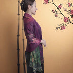 Woman in a traditional outfit standing next to bamboo and a floral branch on a gold background