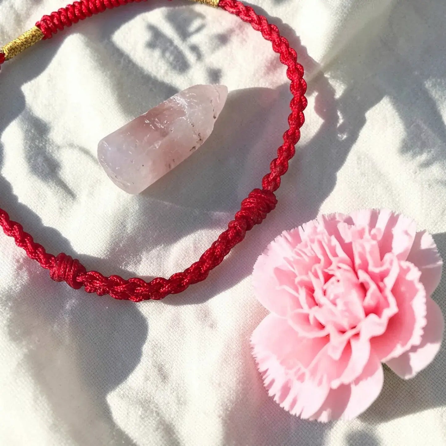 Red braided cord with a pink stone and pink flower on a white fabric background