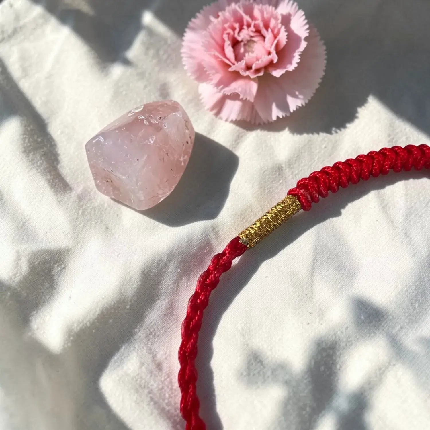 Red cord with gold accent, pink crystal, and pink flower on a textured white surface