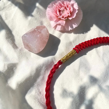 Red cord with gold accent, pink crystal, and pink flower on a textured white surface
