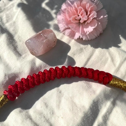 Red and gold beaded bracelet with a pink stone and flower on a textured surface