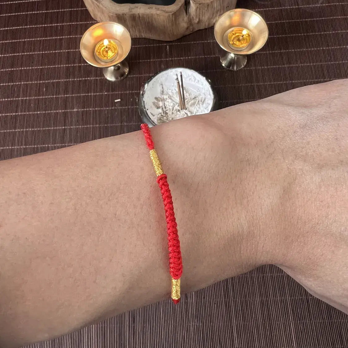 Red bracelet on a wrist with candles and a statue in the background