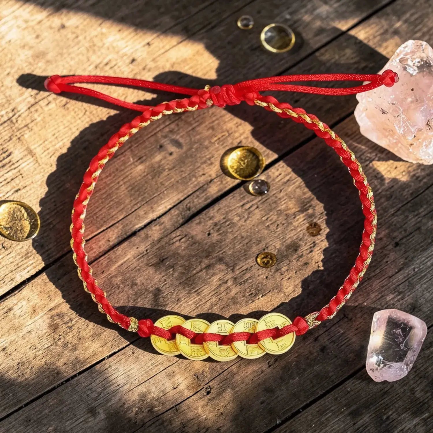 Red cord bracelet with gold coins on a wooden surface