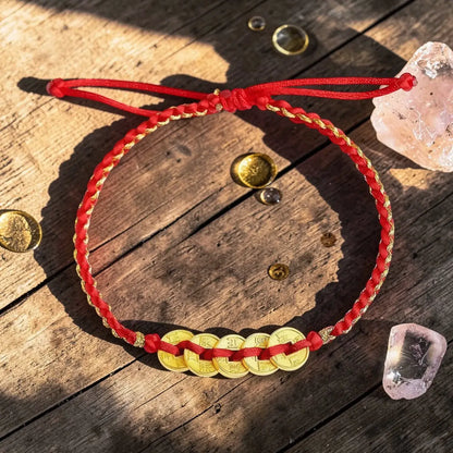Red cord bracelet with gold coins on a wooden surface