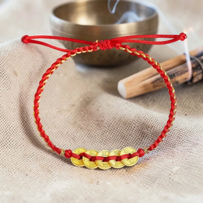 Red and gold bracelet on a textured surface with a metal bowl and wooden stick in the background.