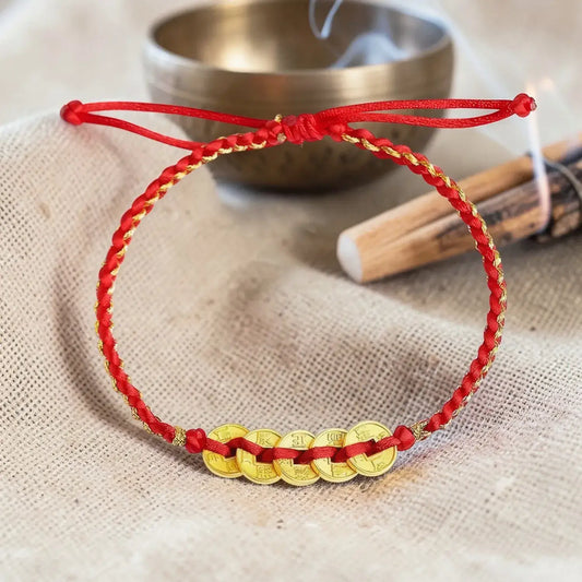 Red and gold bracelet on a textured surface with a metal bowl and wooden stick in the background.