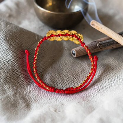 Red and gold bracelet on a textured fabric background with a singing bowl and wooden stick.