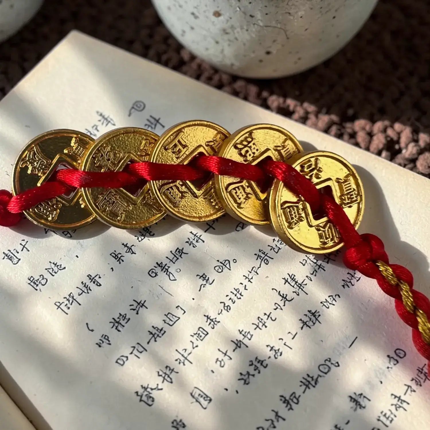 Gold coins on a red string bracelet on an open book with Chinese text.