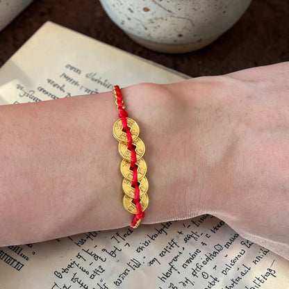 Gold bracelet with red cord on a wrist, placed on an open book.