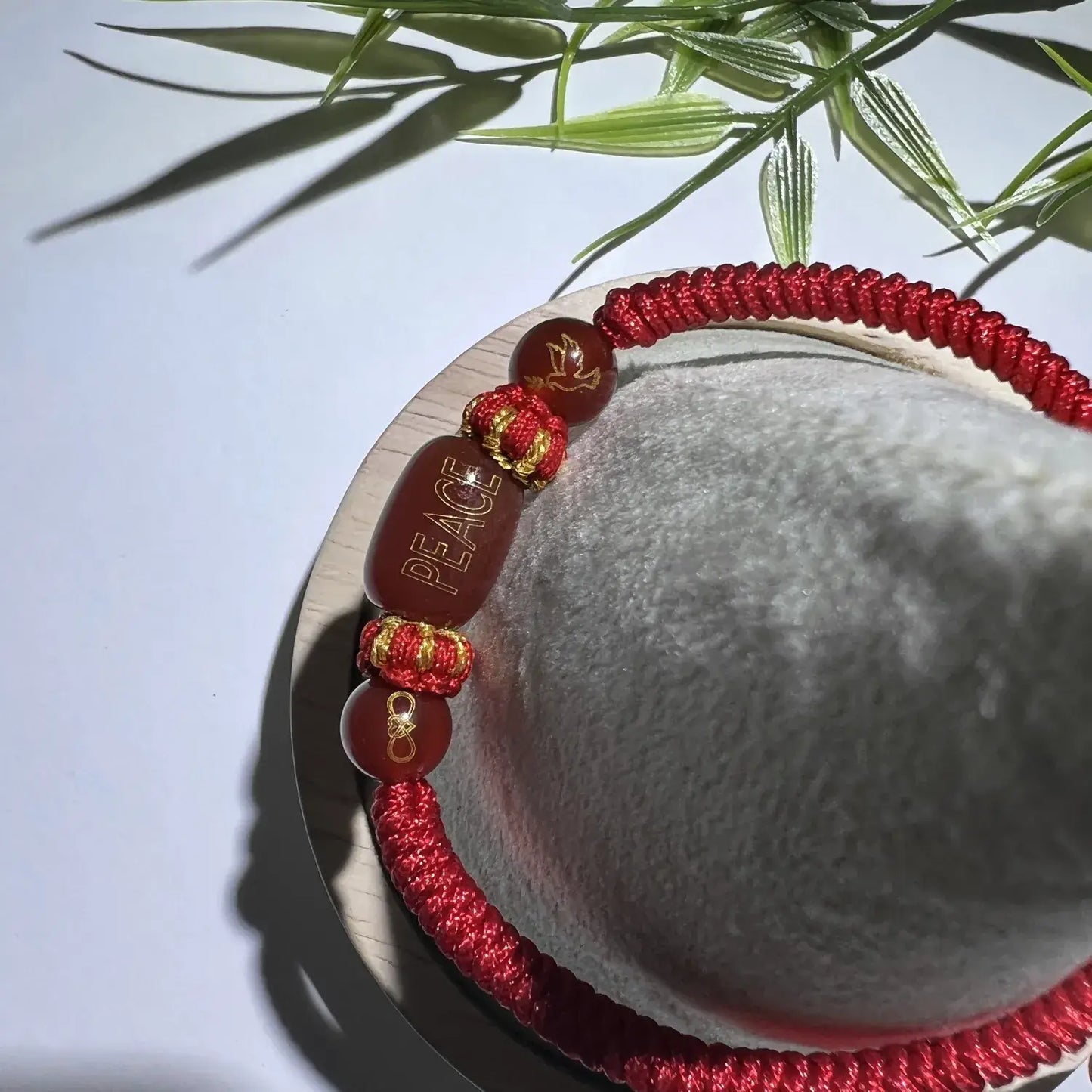 Red bracelet with gold accents on a white surface with green leaves in the background