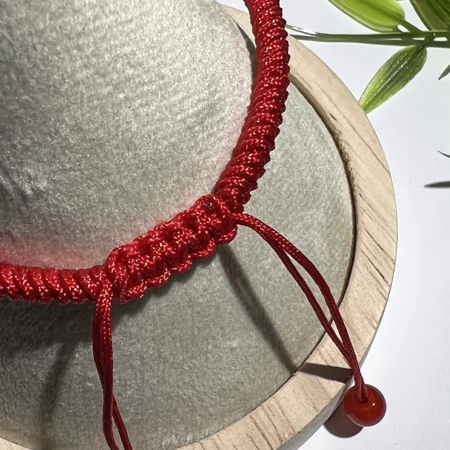 Red braided bracelet with a red bead on a stone surface