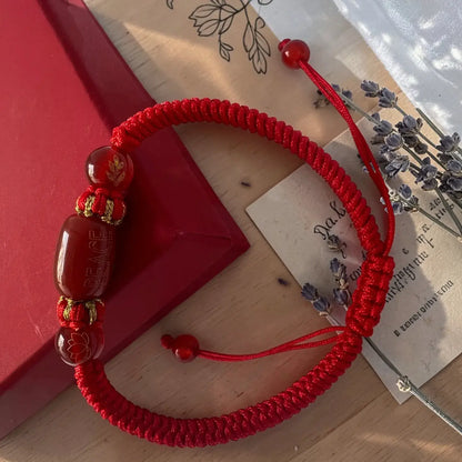 Red bracelet with beads on a wooden surface with a red envelope and paper in the background.