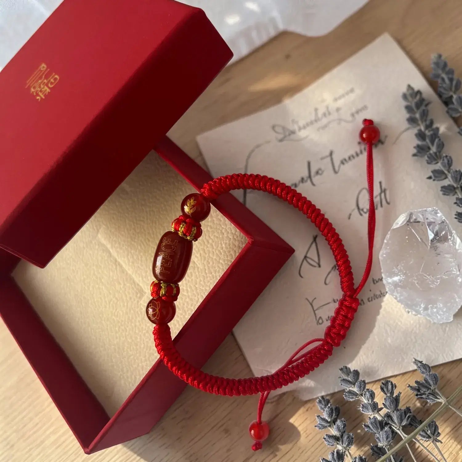 Red string bracelet with beads on a wooden surface with a red box and card.