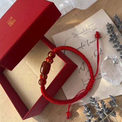 Red string bracelet with beads on a wooden surface with a red box and card.