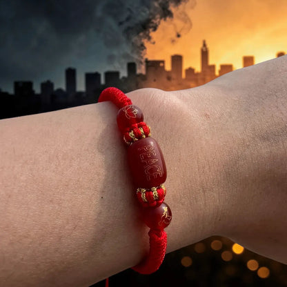 Red bracelet with 'PEACE' beads on a wrist against a cityscape background