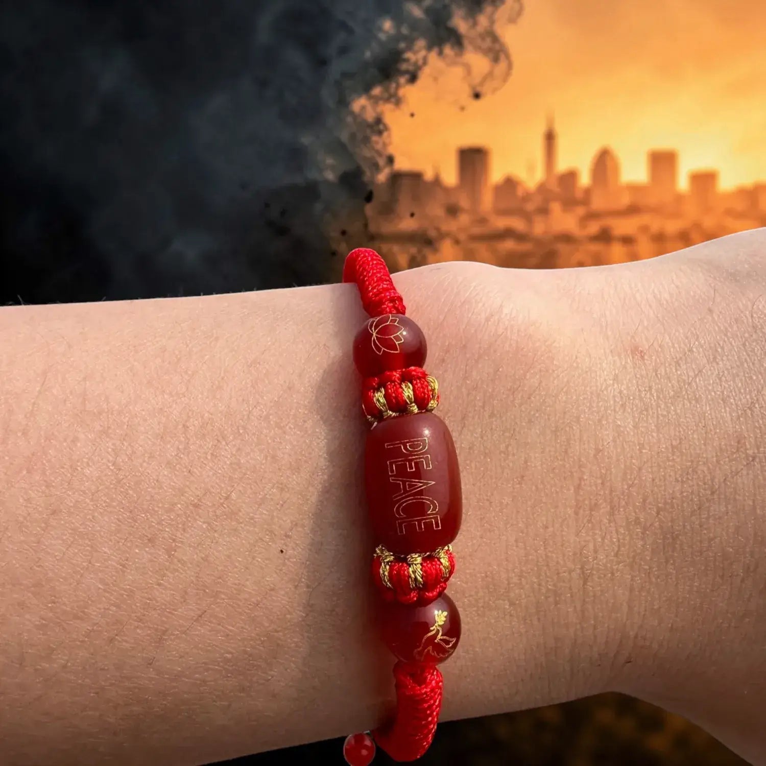 Red beaded bracelet with 'PEACE' on wrist against a cityscape with smoke in the background