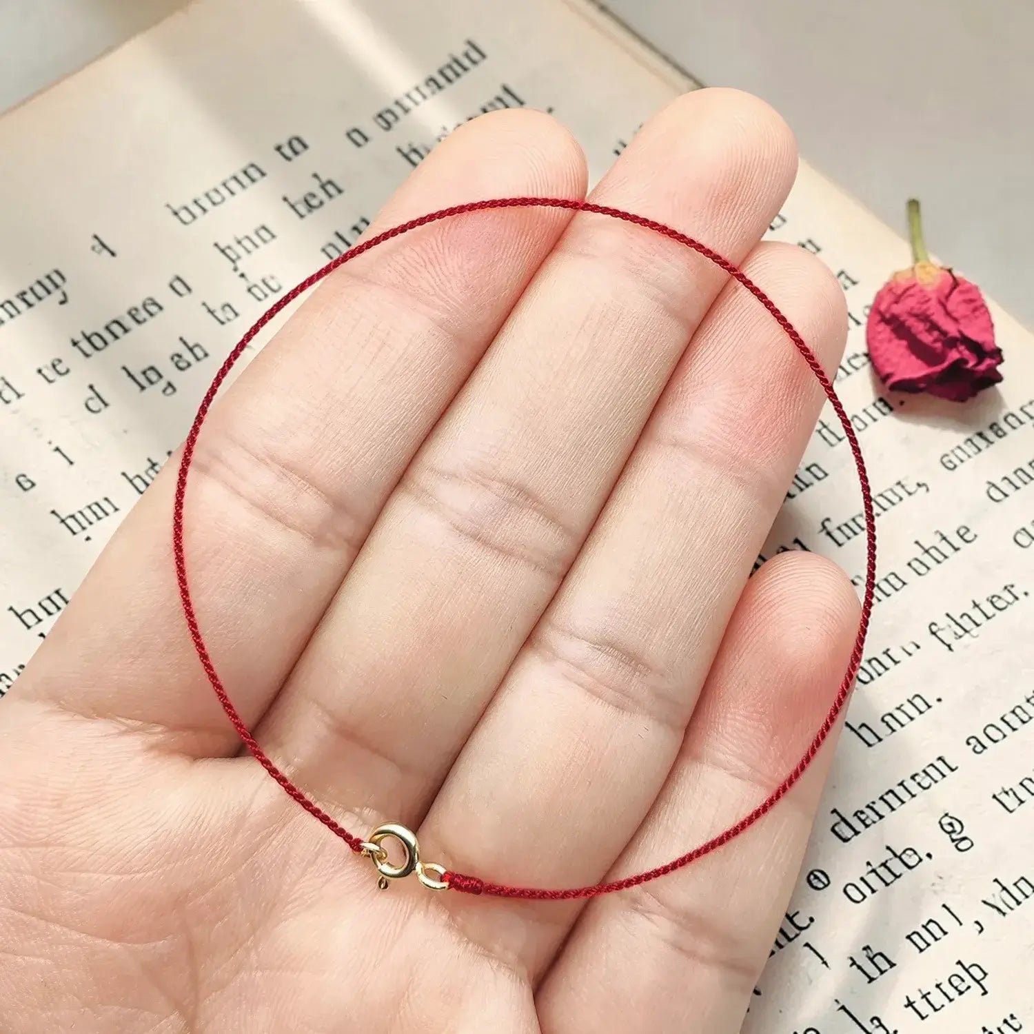 Red string bracelet on a hand with a book and dried flower in the background